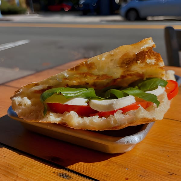 A Pan and Peel Pizza Caprese sandwich with fresh mozzarella, tomatoes, and basil on a wooden table.