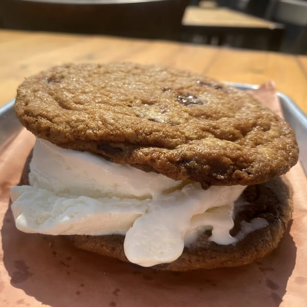 A large ice cream sandwich with vanilla ice cream between two chocolate chip cookies on a tray.