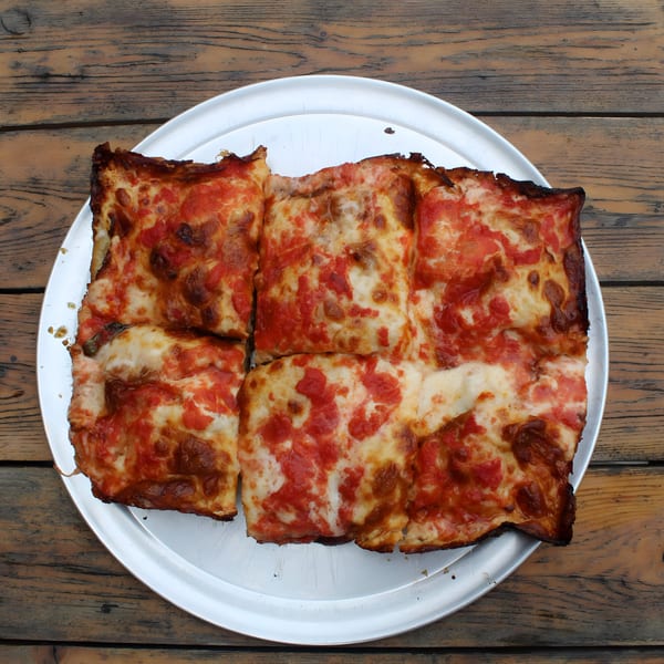 Four square slices of Pan and Peel Pizza's Detroit-style pizza with red sauce and cheese on a metal tray.