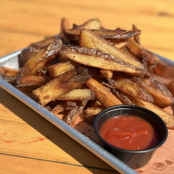 Crispy, golden-brown french fries with salt, served in a metal tray with a side of ketchup.