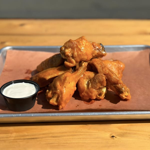 Buffalo chicken wings with a side of ranch dressing on a metal tray with brown paper.